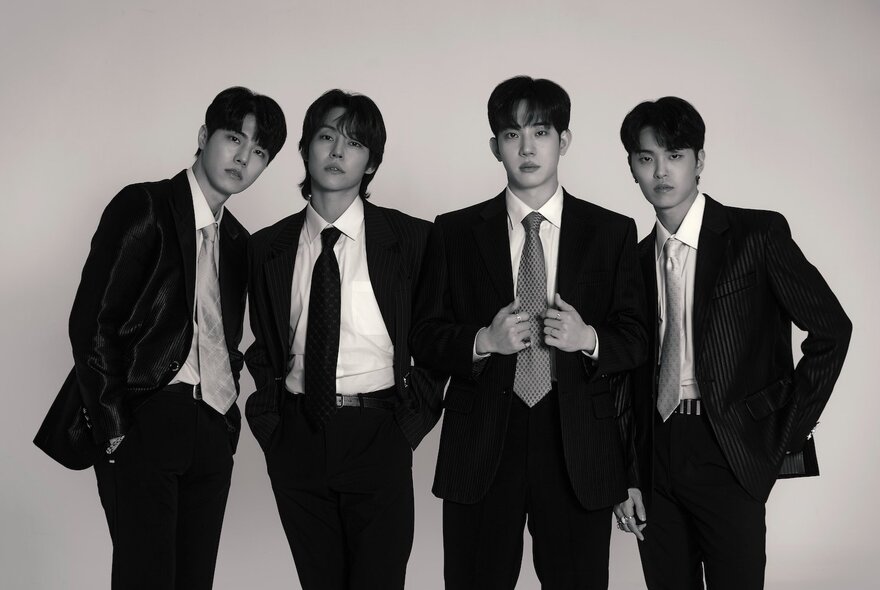 Black and white photograph of the four members of the Korean rock band, The Rose, wearing black suits and ties.