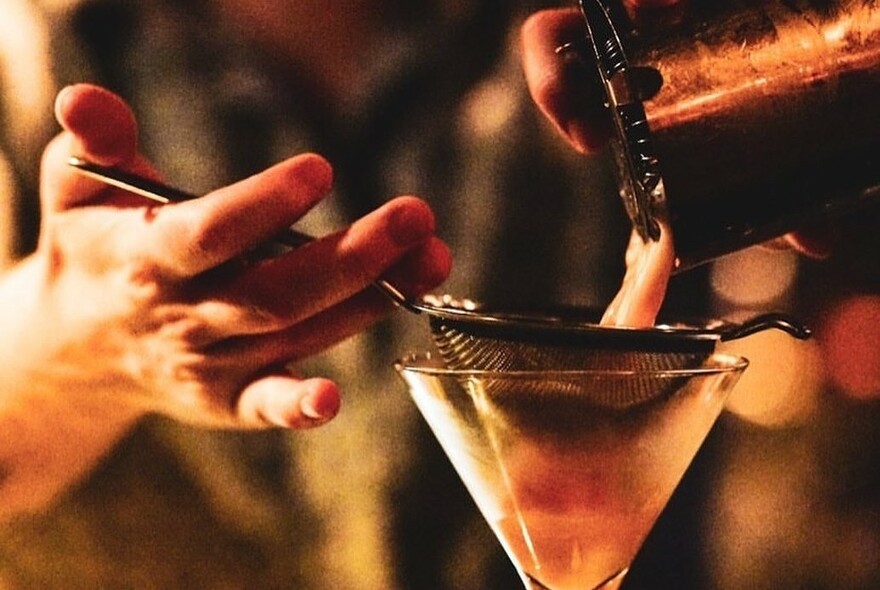 Person pouring a cocktail through a strainer.