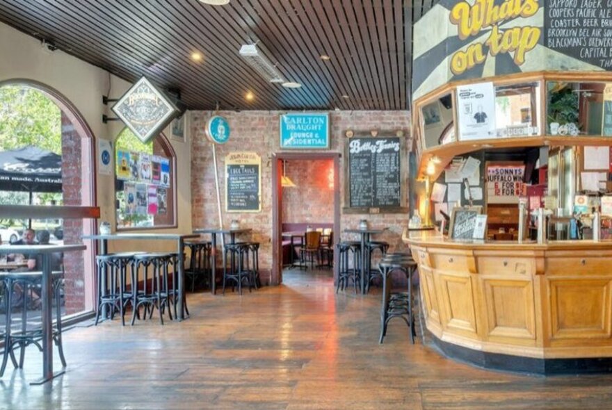 Pub interior with large wooden bar, stool seating and signage.