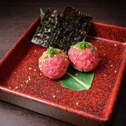 Two beef tartare meatballs with seaweed on a red plate.