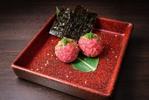 Two beef tartare meatballs with seaweed on a red plate.