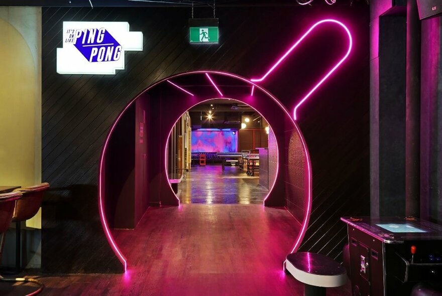 Circular doorway illuminated with pink neon and a ping pong sign.