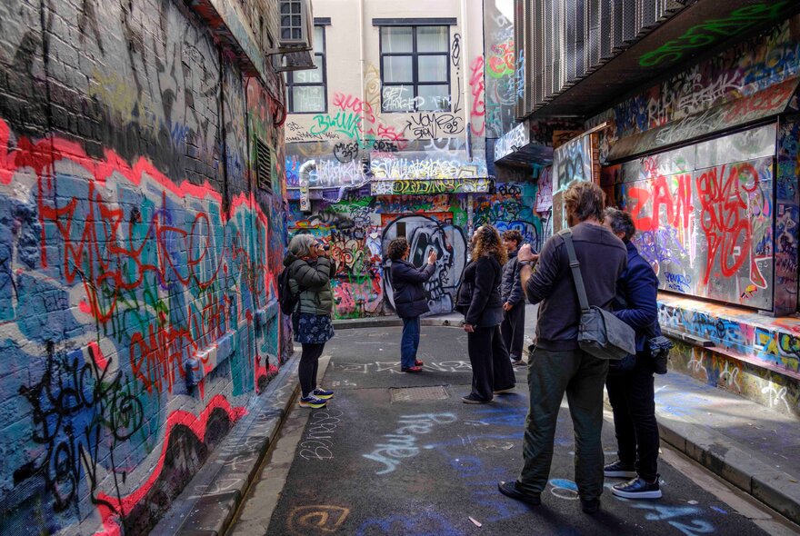 Camera group standing in a laneway daubed with graffiti tags.
