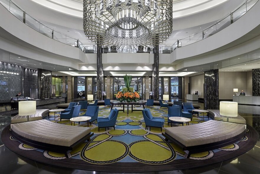 Hotel foyer with reception areas, bench and chair seating, central light sculpture and tiered walkways circling above.