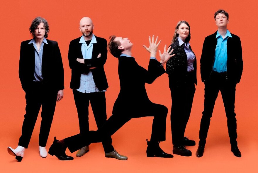 The five members of the band Franz Ferdinand, all wearing black suits and posed against an orange background. 