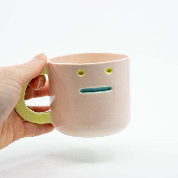 A ceramic mug with a face on it with a straight mouth. 