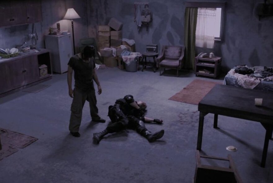 A still from the film The Raid showing a body on a floor of a dark room with a person standing over them. 