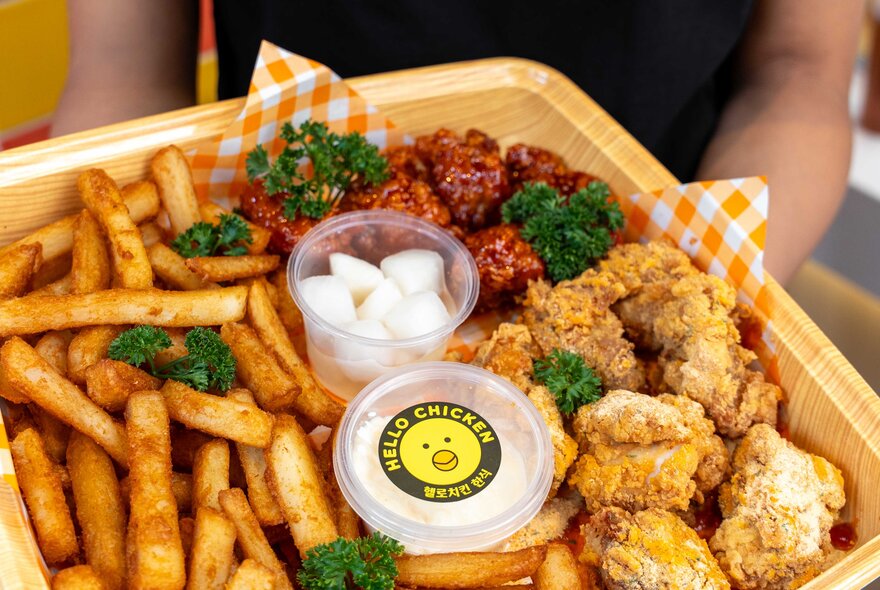 A square tray of Korean fried chicken and thick-cut chips, with two small containers of sauce in the centre.