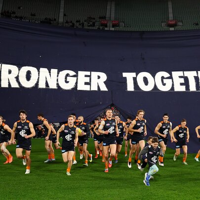 Carlton AFL football team running through a 'Stronger Together' flag at the start of a match.