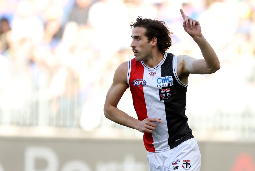 A St Kilda AFL player running on the field with one hand raised above with finger pointing in a victory gesture.