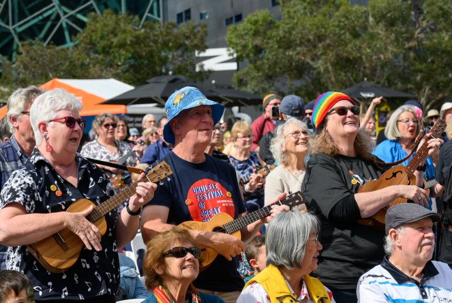 A bunch of older people playing ukelele together, outdoors at Melbourne's Fed Square.