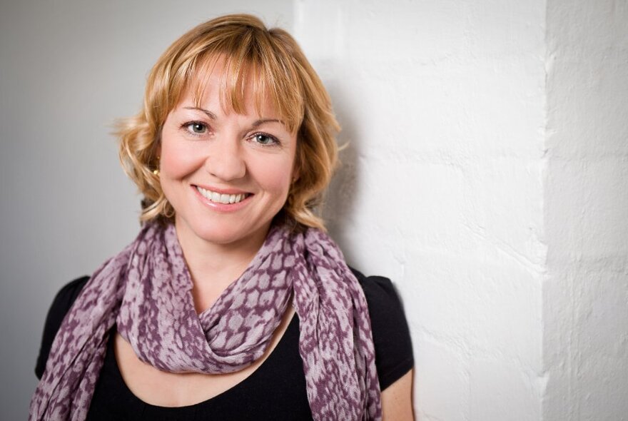 Portrait of children's author, Nicole Hayes, in front of a white-painted brick wall.