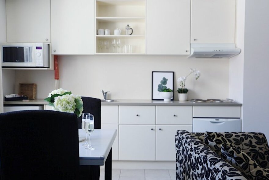 The kitchen of a serviced apartment, with a patterned couch and dining table in the foreground.