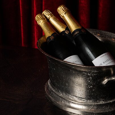 Three champagne or sparkling wine bottles chilling in an antique-style metal ice bucket.