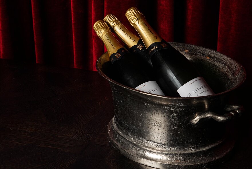 Three champagne or sparkling wine bottles chilling in an antique-style metal ice bucket.