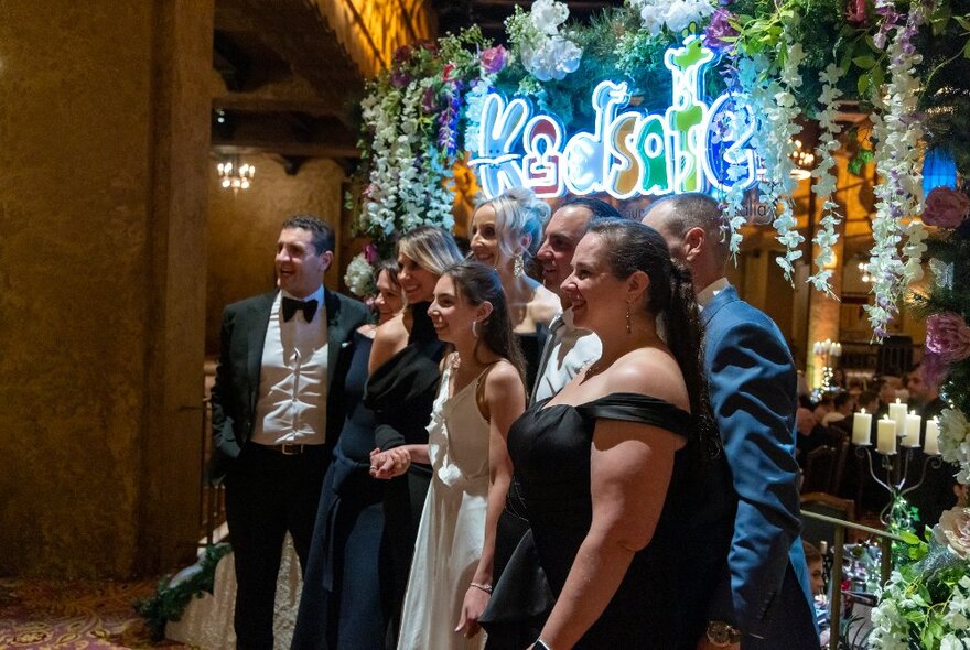 People wearing formal wear lined up on a stage with signage and flowers.