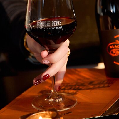 A woman's hand holding the stem of a large red wine glass.
