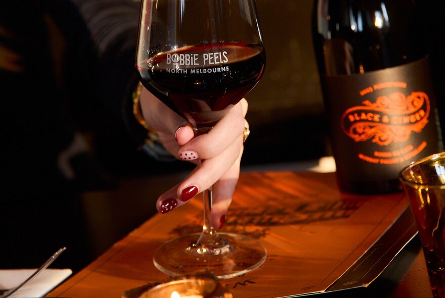 A woman's hand holding the stem of a large red wine glass.