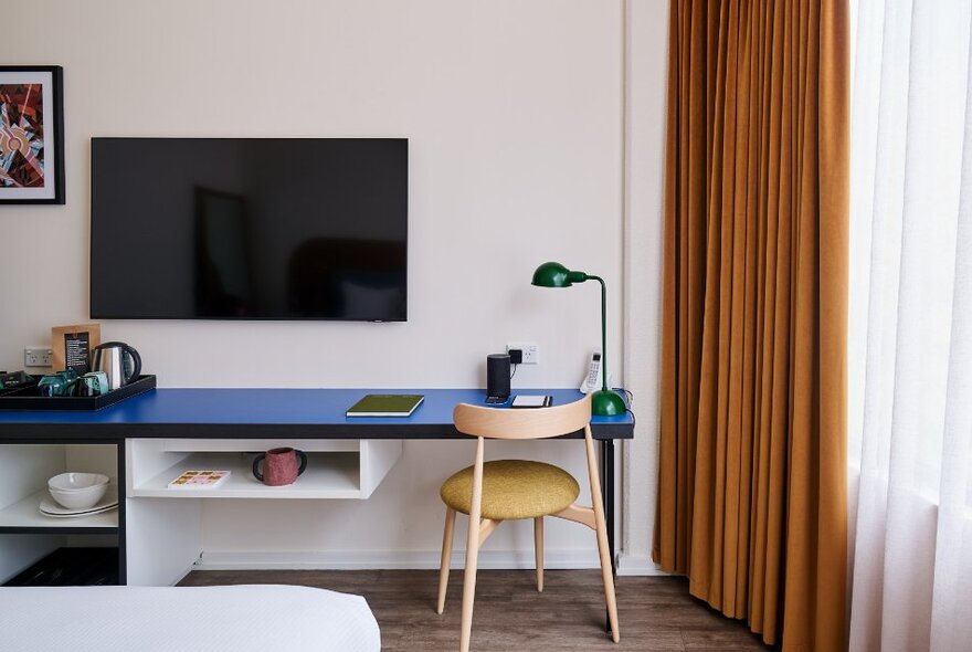 Interior of a hotel room showing a desk space and tv on the wall. 