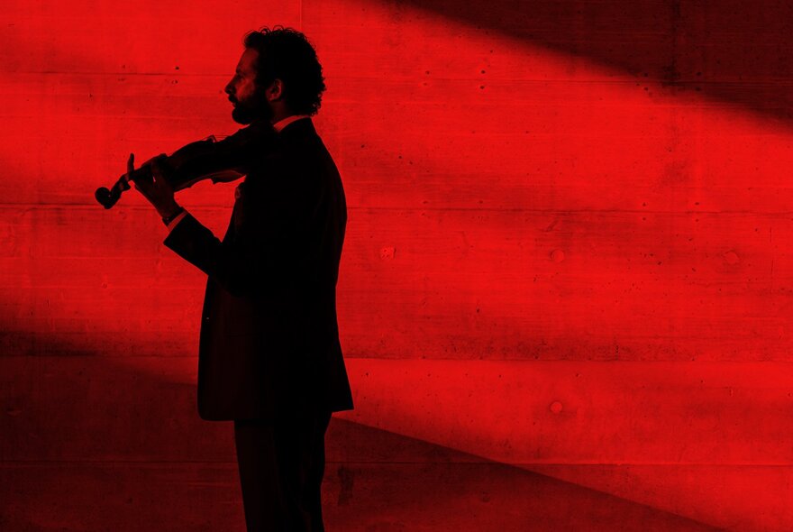 Violinist Ilya Gringolts in a side-angled silhouette in a red filtered image. 