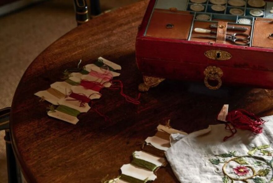 Embroidery threads and work on a wooden table with an antique wooden sewing box.