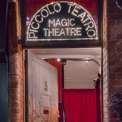 The entrance to the Piccolo Teatro Magic Theatre with a neon sign above the rustic wooden door.