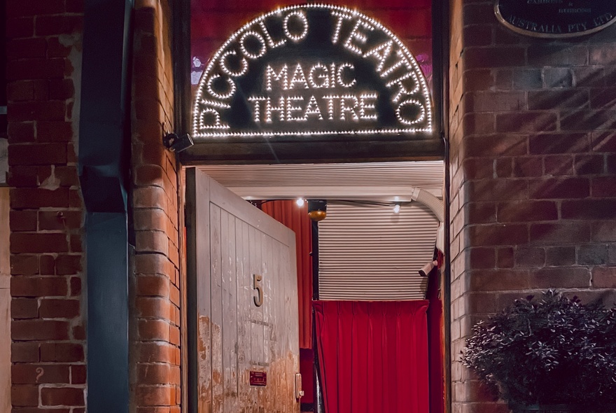 The entrance to the Piccolo Teatro Magic Theatre with a neon sign above the rustic wooden door.