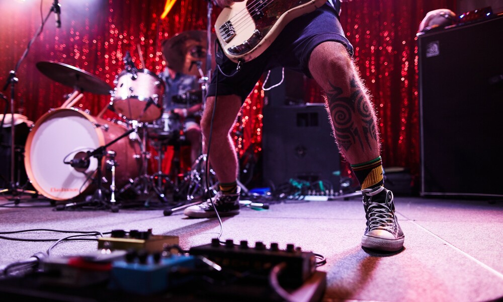 Close-up shot of a stage with a guitarist's legs and a drum set.  