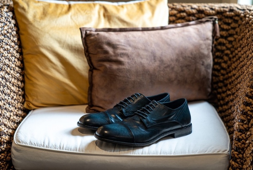 Black leather shoes on cane chair with yellow and brown cushions.