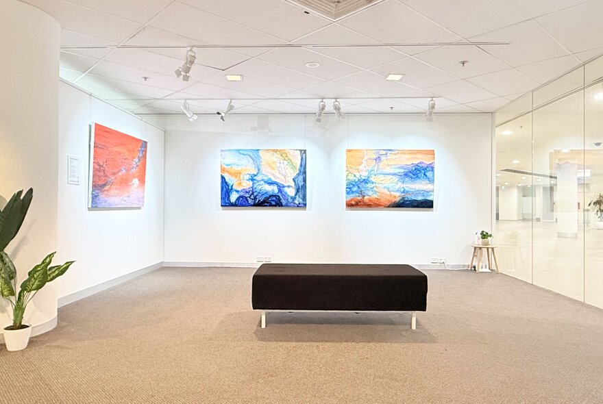 Gallery space with central bench seat, large abstract paintings displayed on white walls.