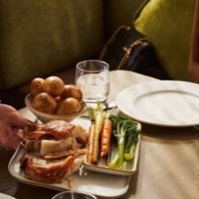 A plate of roast pork and side dish of vegetables being placed on a table. 
