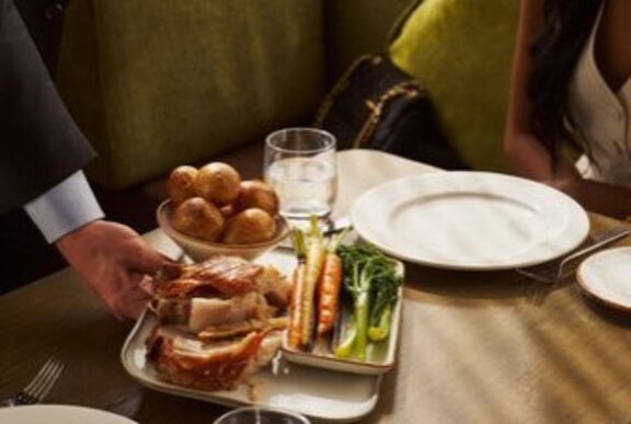 A plate of roast pork and side dish of vegetables being placed on a table. 