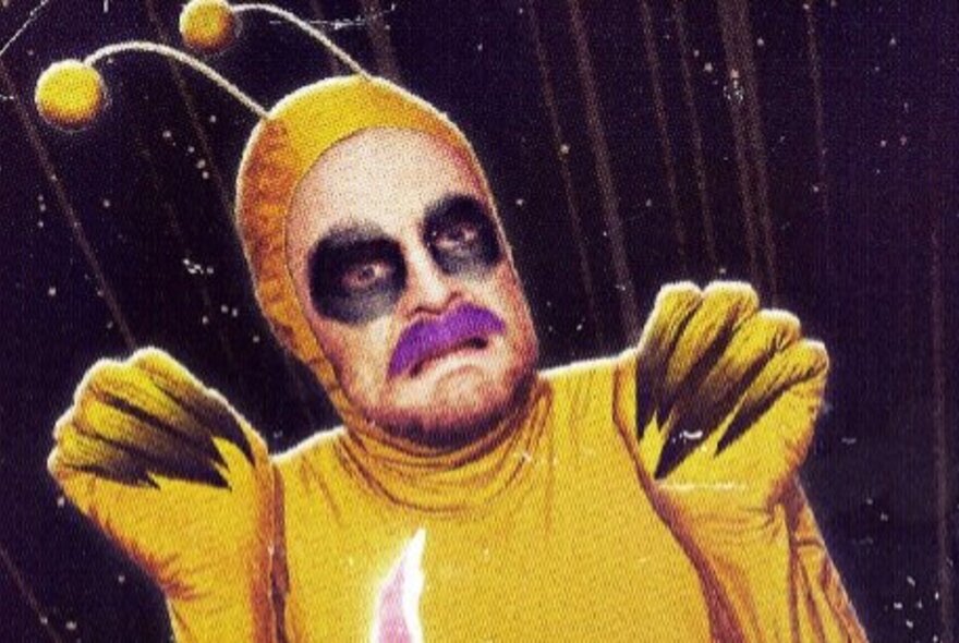 Man dressed in yellow alien outfit with feelers, claws and black eyes.