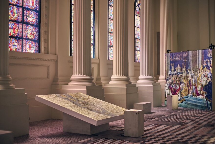 A large print of a colourful painting depicting the crowning of a monarch, inside a large room with checked carpet and marble pillars.