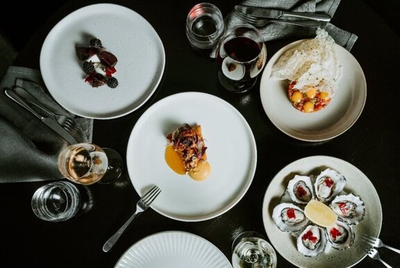 Looking down at a table with three white plates of carefully arranged food, and glasses of wine.