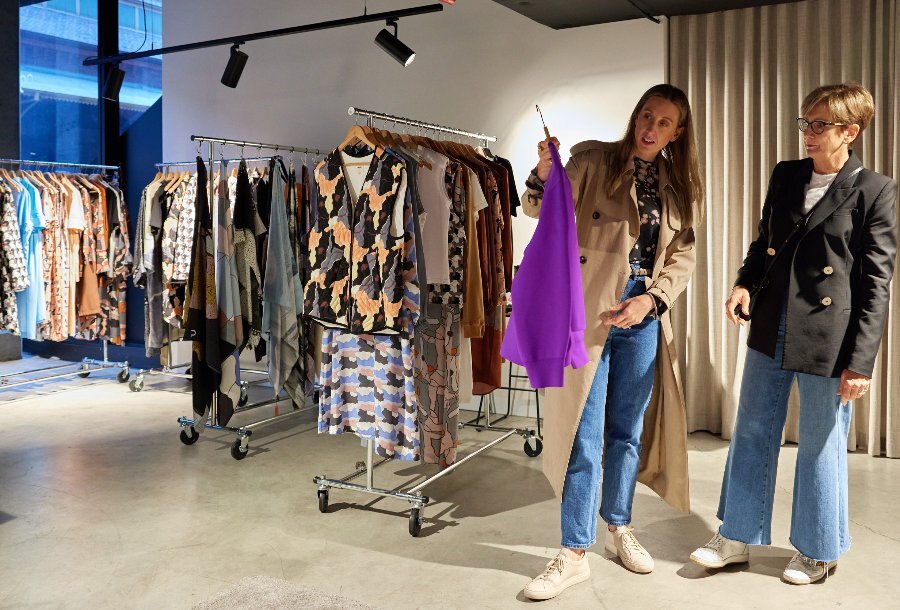 Two women are in a clothing store looking at a purple top
