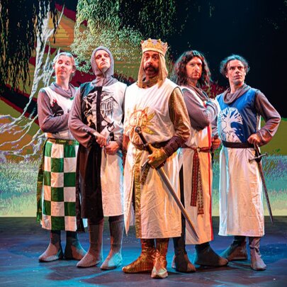 King Arthur and knights standing on stage in medieval dress.