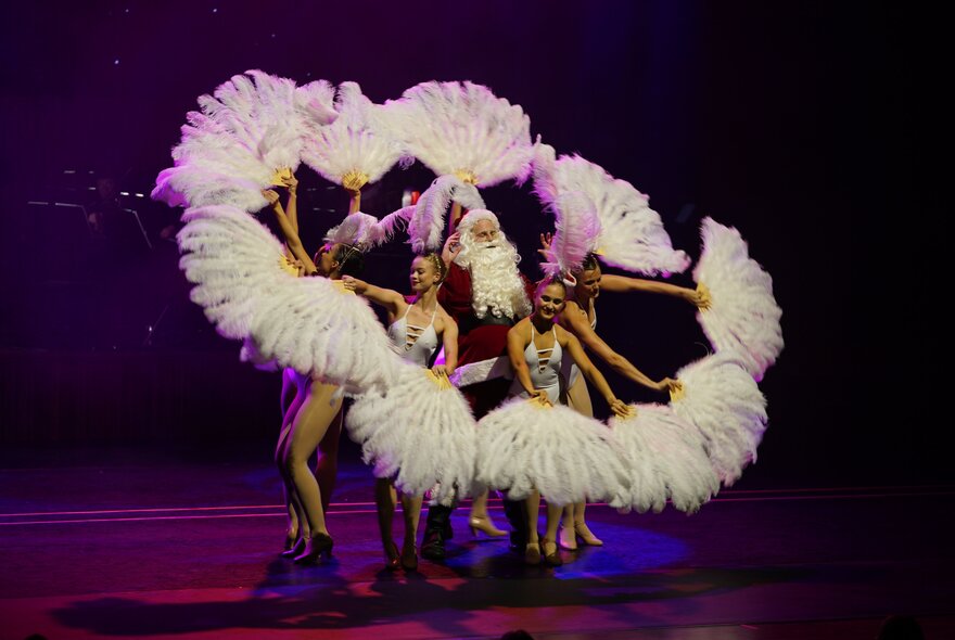 Dancers holding feather fans in a circle on stage.