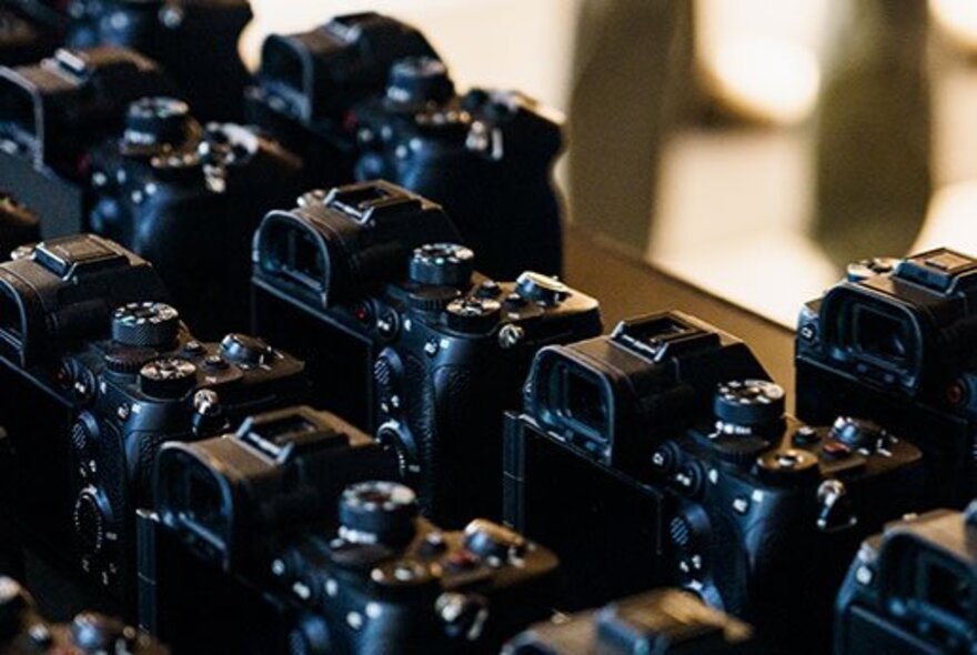 Multiple black SLR cameras arranged on a table at an expo.