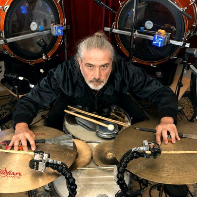 A percussion musician surrounded by an enormous drumkit, with his hands on the cymbols.