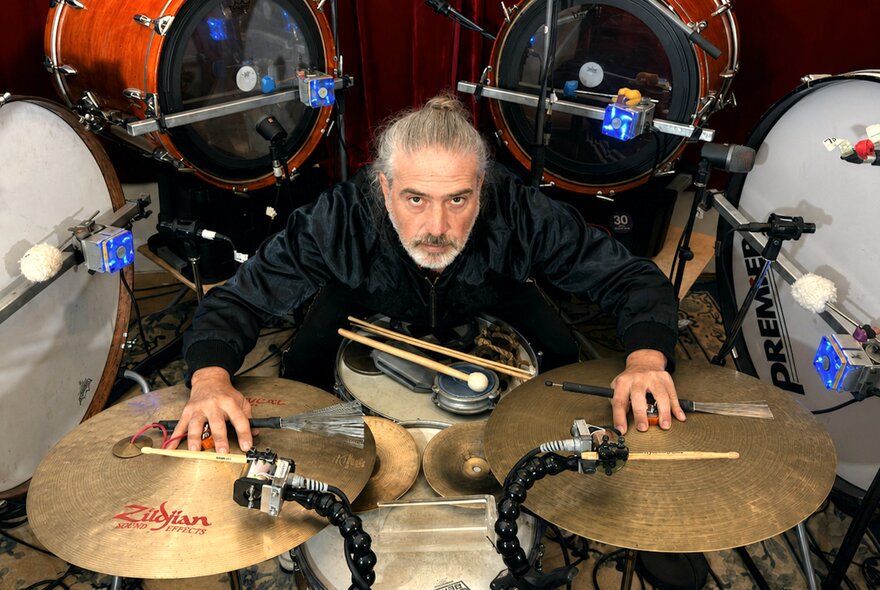 A percussion musician surrounded by an enormous drumkit, with his hands on the cymbols.