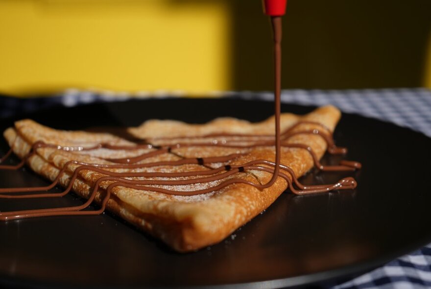 A classic triangular shaped French crepe being drizzled with chocolate sauce. 