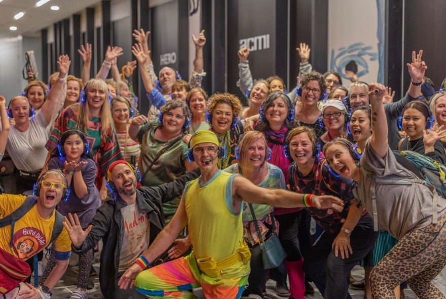 Group of people wearing headphones and posing with their arms raised in the air above their heads in a dance-style move, in front of ACMI cinema in Melbourne city.