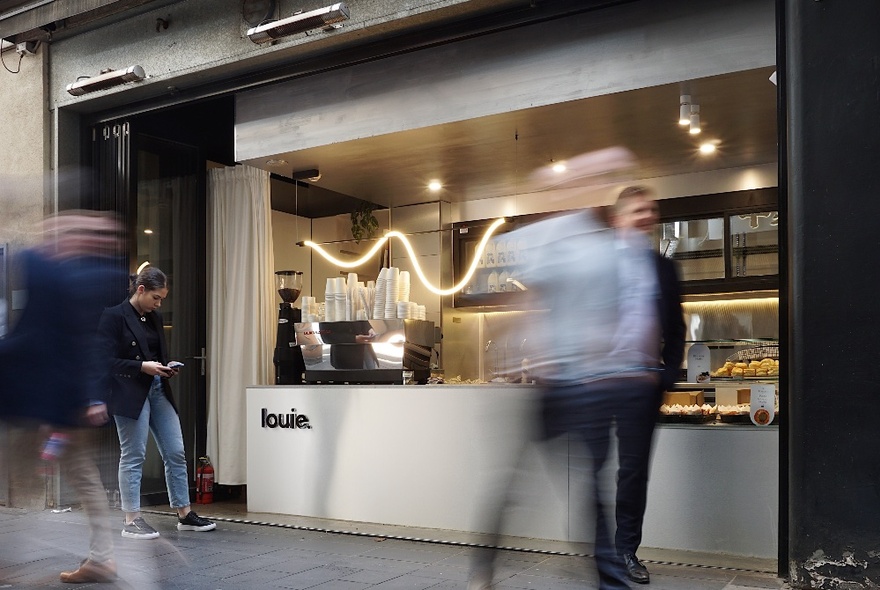 A blurred motion picture showing a woman waiting in front of a small cafe counter with men also waiting. 