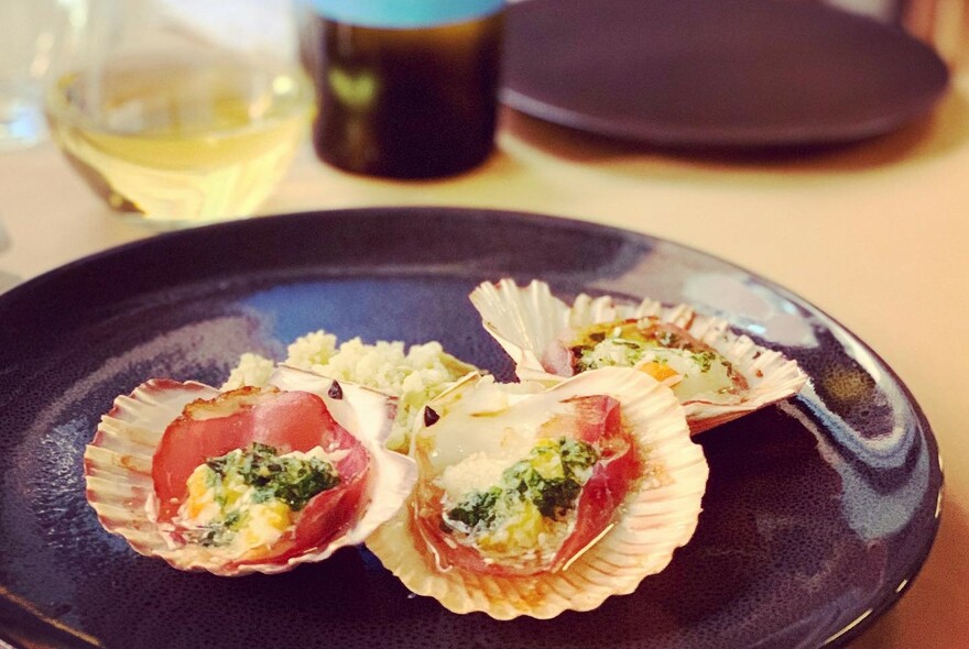 A plate with three scallops and a glass of white wine in the background.