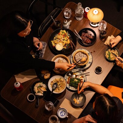 Looking down on a table from a height at diners eating from many small plates with chopsticks. 