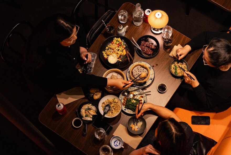Looking down on a table from a height at diners eating from many small plates with chopsticks. 