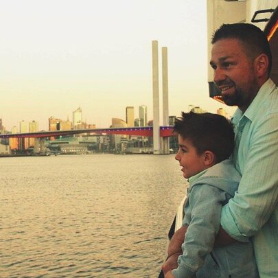 A father and his young son standing on a boat deck and admiring the view of Melbourne's harbour.