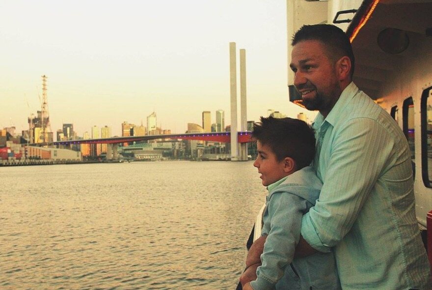 A father and his young son standing on a boat deck and admiring the view of Melbourne's harbour.