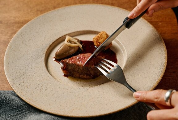 A restaurant plate with someone cutting into a piece of rare beef.